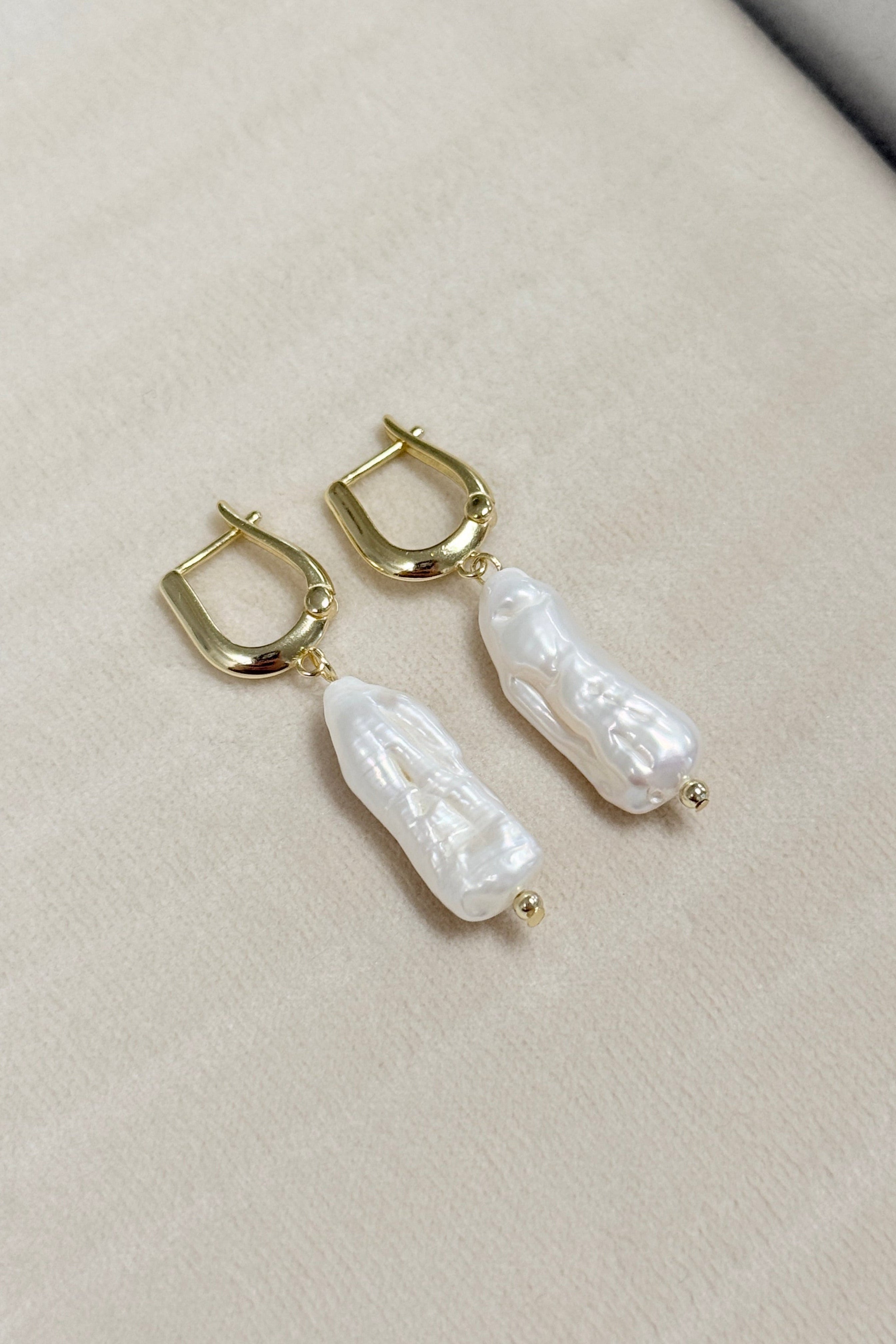 Pearl earrings with gold hooks on a light gray surface