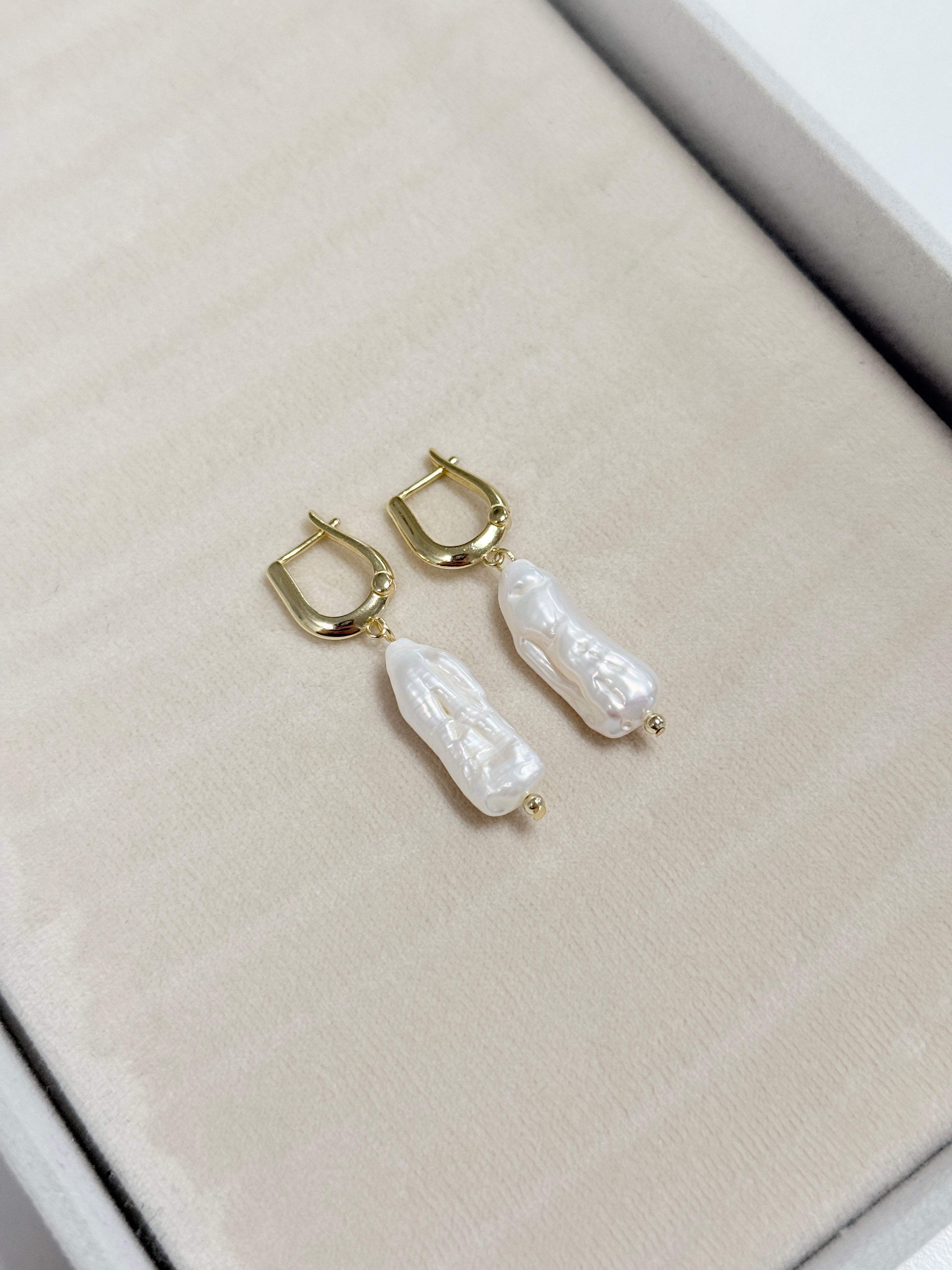 Pearl earrings with gold hooks on a light gray surface
