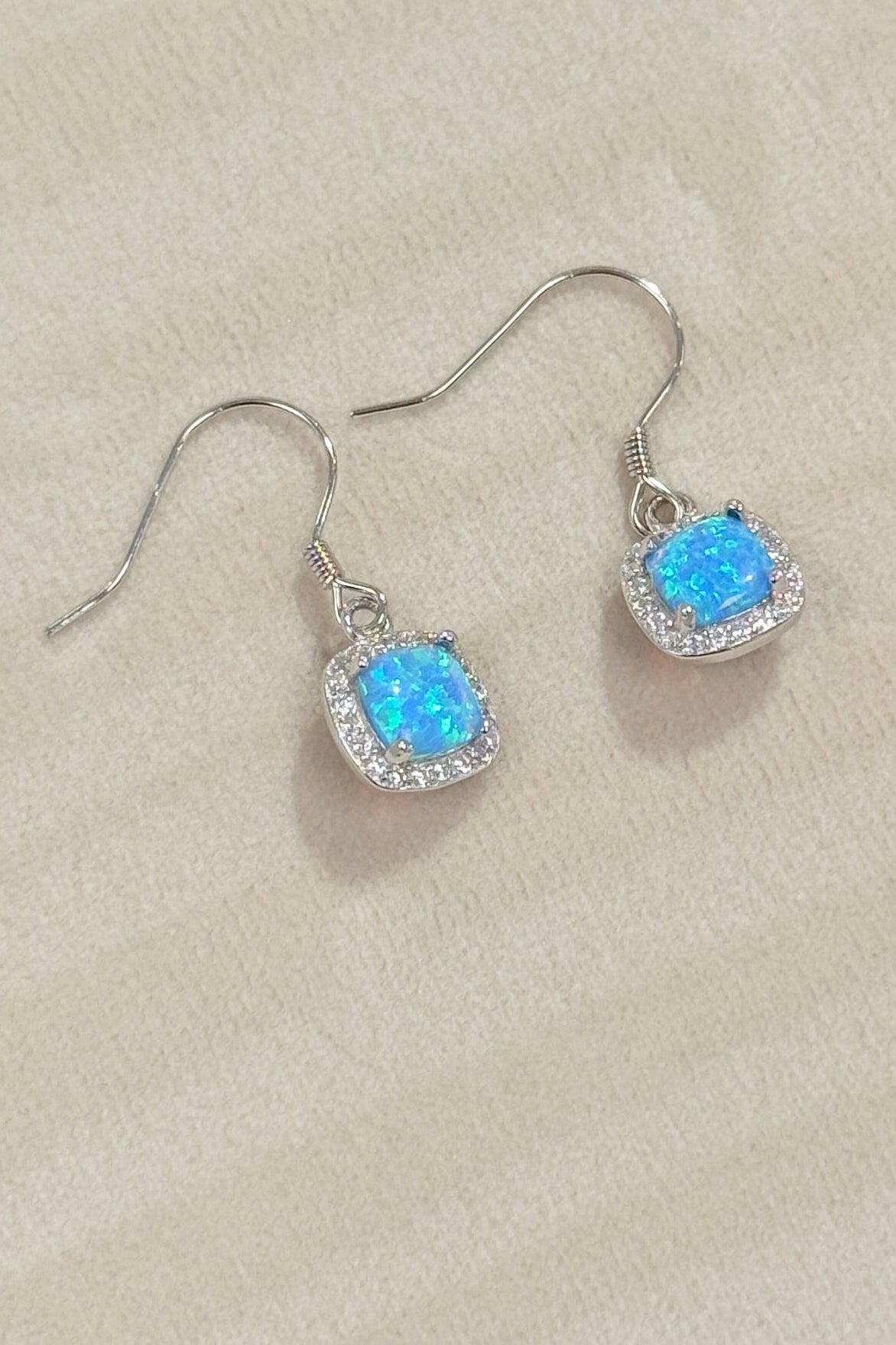Pair of silver earrings with blue gemstones on a beige jewelry box.