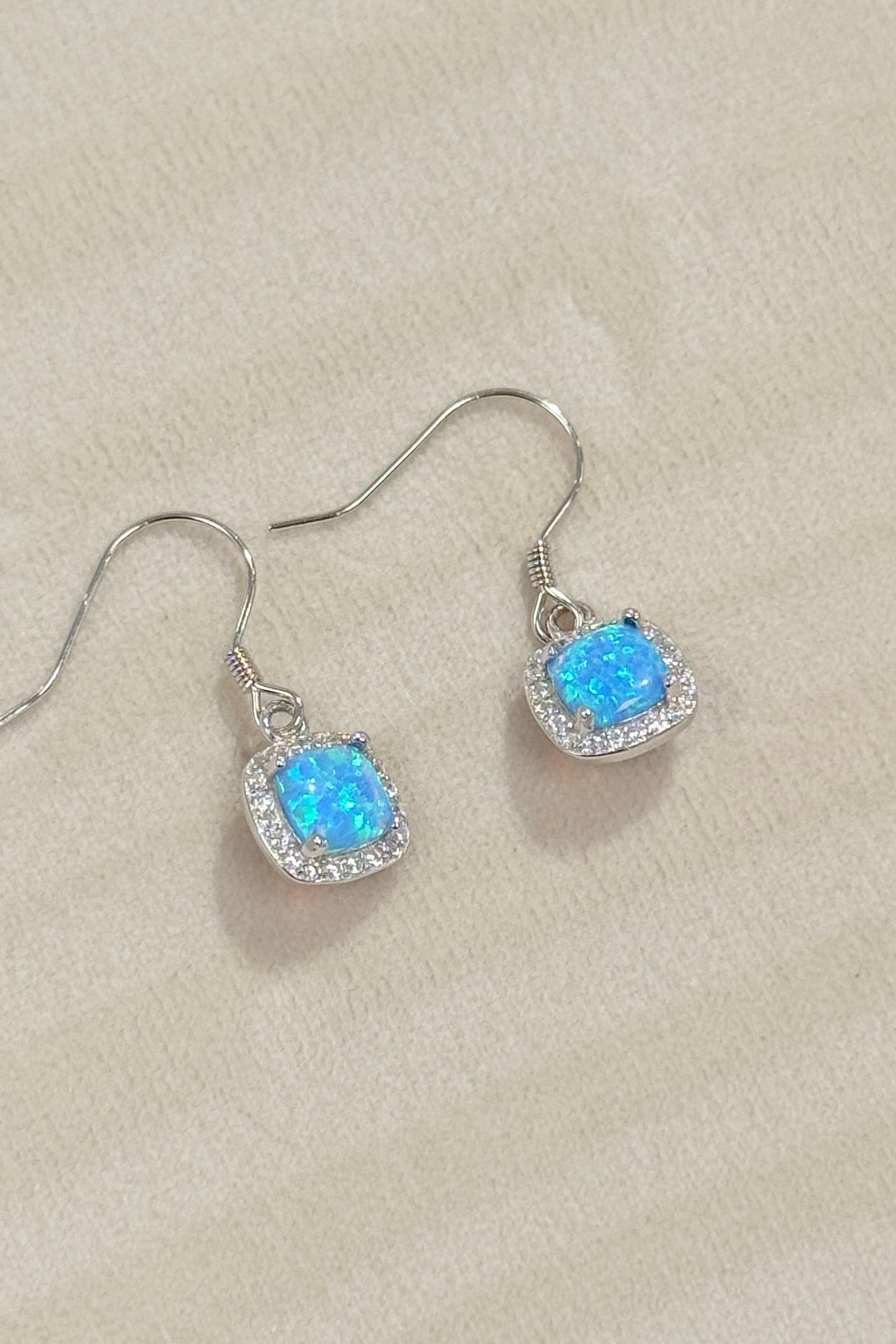 Pair of silver earrings with blue gemstones on a beige jewelry box.