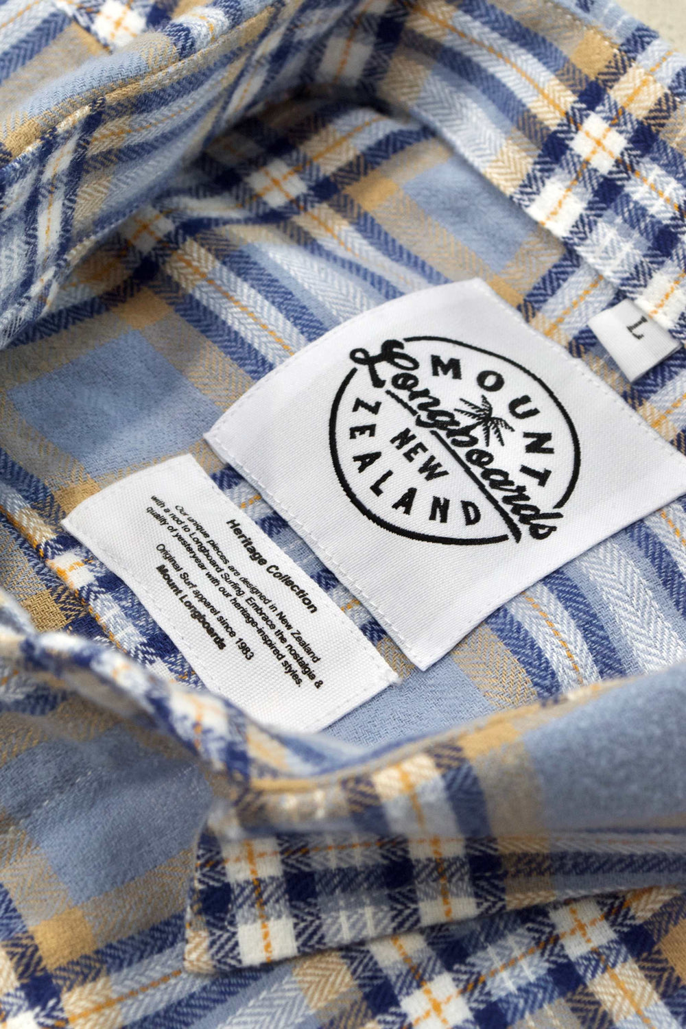Blue plaid flannel shirt with Mountain New Zealand label and diamond logo, showcasing durable and soft cotton fabric in Fjord style.